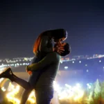 Couple embracing at sunset with city skyline lights in the background